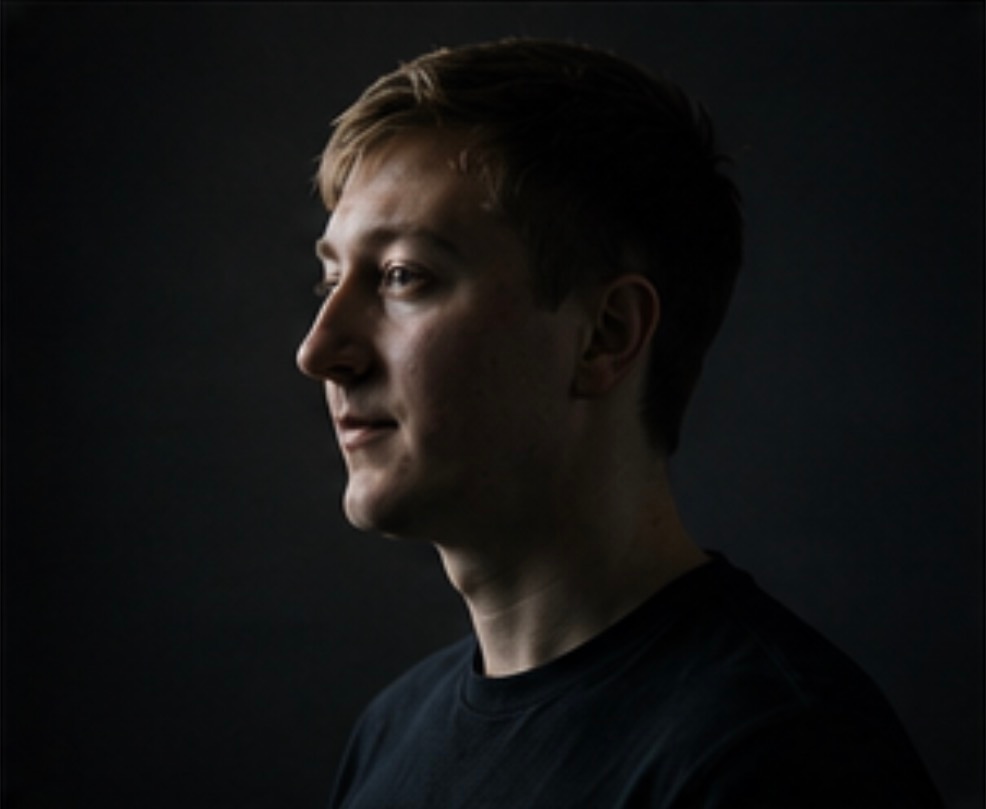 Side-profile portrait of Moritz Zinecker against a dark background