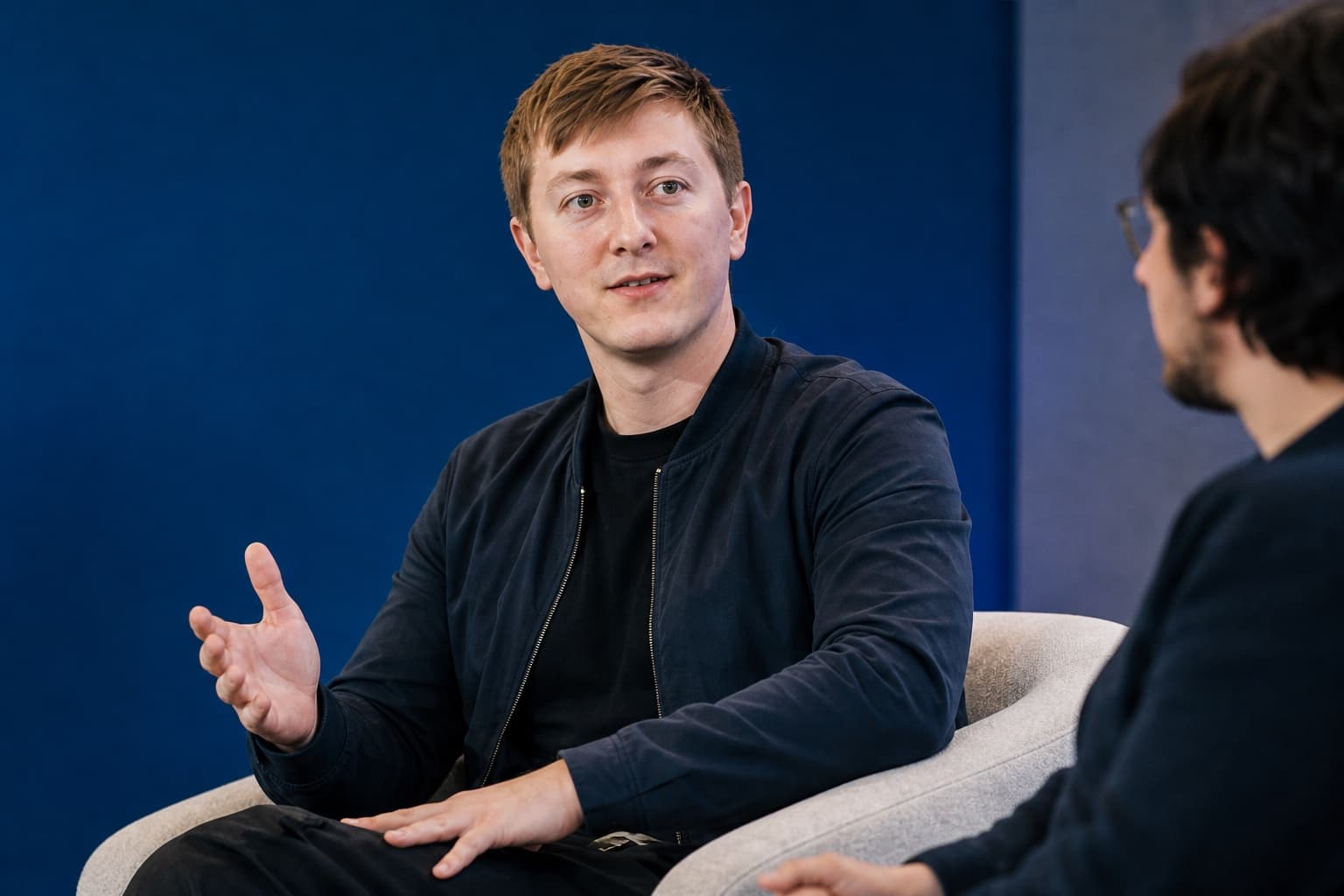 Moritz Zinecker gesturing during a seated conversation on a blue stage
