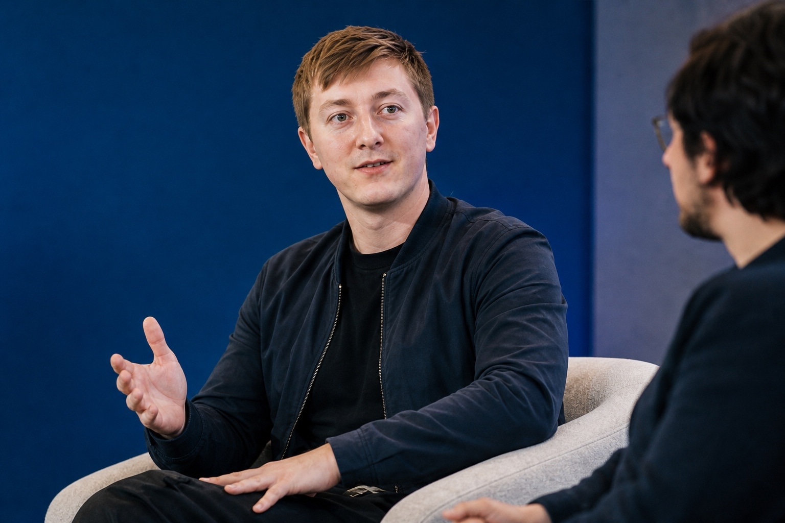 Moritz Zinecker gesturing during a seated conversation on a blue stage