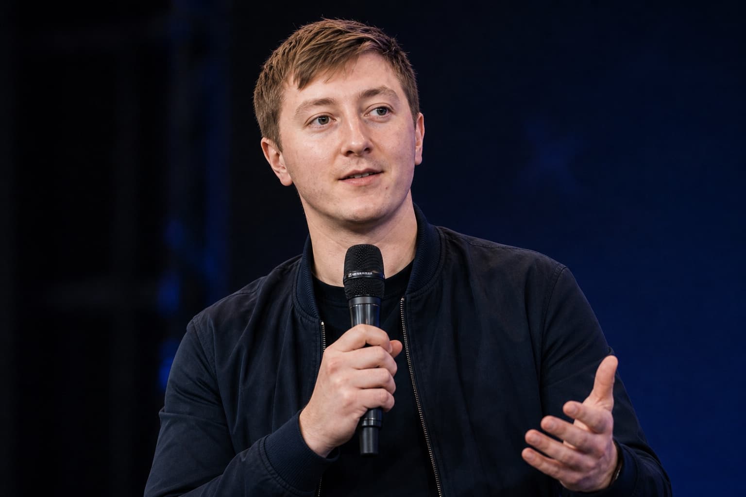 Moritz Zinecker speaking with a handheld microphone on a dark stage